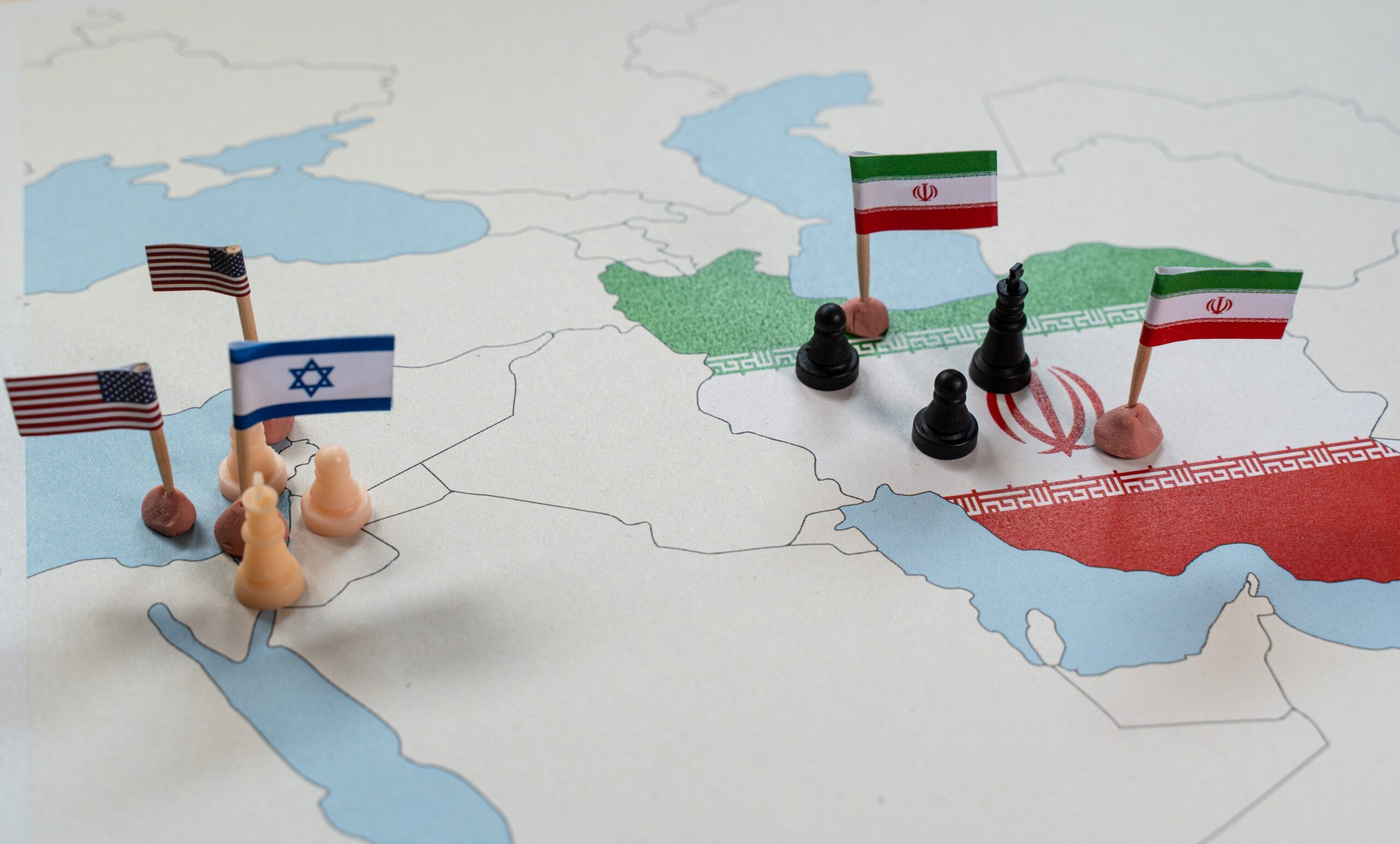 نقشه جغرافیایی از غرب آسیا با مهره های شطرنج و پرچم های ایران، اسرائیل و آمریکا