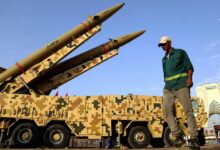 دو فروند موشک بالستیک ذوالفقار روی پرتابگر متحرک با استتار دیجیتالی در میدان آزادی تهران با حضور یک عابر پیاده.
