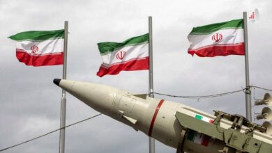 سه پرچم در حال اهتزاز ایران در پس‌زمینه آسمان ابری همراه با کلاهک یک موشک نظامی در بخش جلویی تصویر