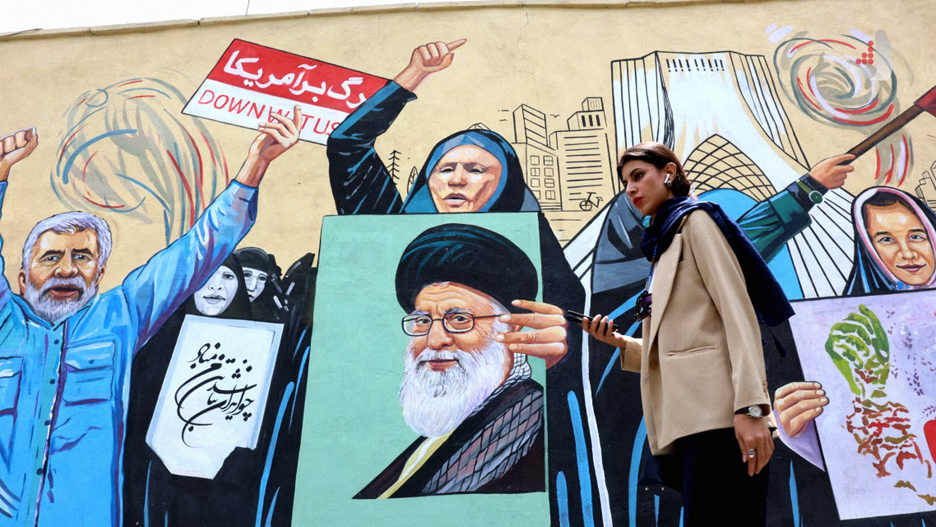 زنی با کت کرم‌رنگ در حال قدم زدن از مقابل یک دیوارنگاره در تهران شامل تصویر شهید آیت‌الله خامنه‌ای و شعار مرگ بر آمریکا