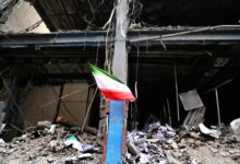 پرچم ایران برافراشته بر روی یک تیر فولادی در میان آوار و ویرانه‌های یک ساختمان تخریب‌شده