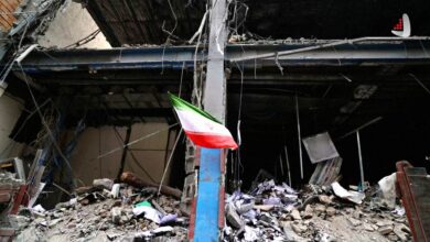 پرچم ایران برافراشته بر روی یک تیر فولادی در میان آوار و ویرانه‌های یک ساختمان تخریب‌شده